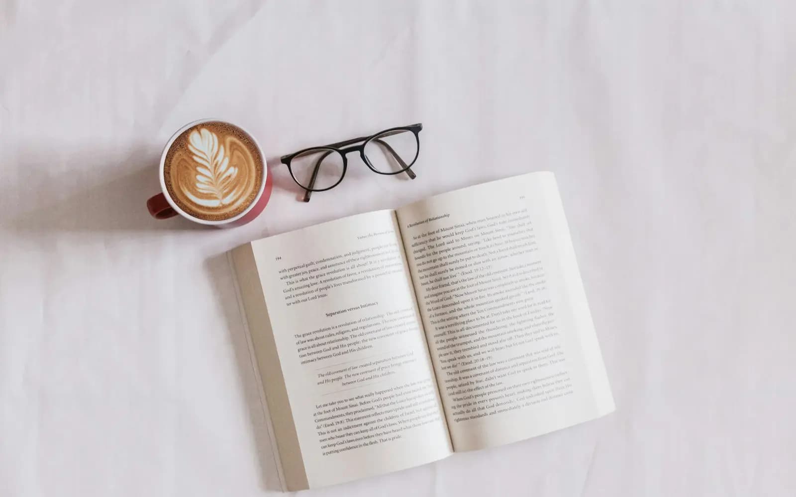 An open book beside a cup of coffee and reading glasses