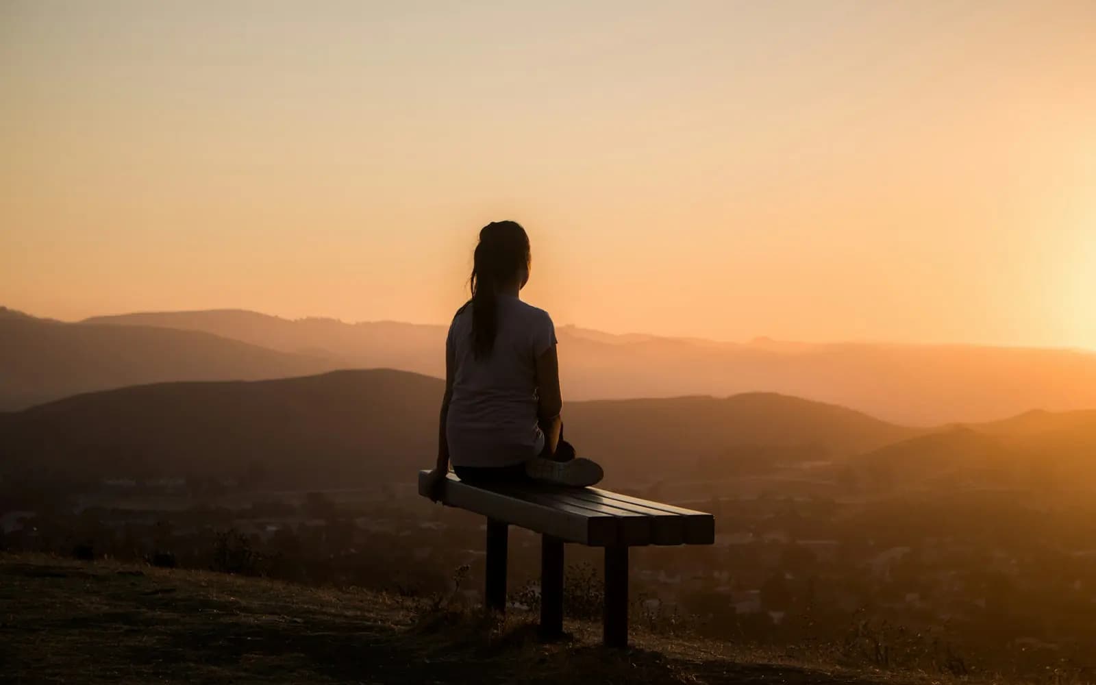 A person sitting on a bench looking out over distant mountains